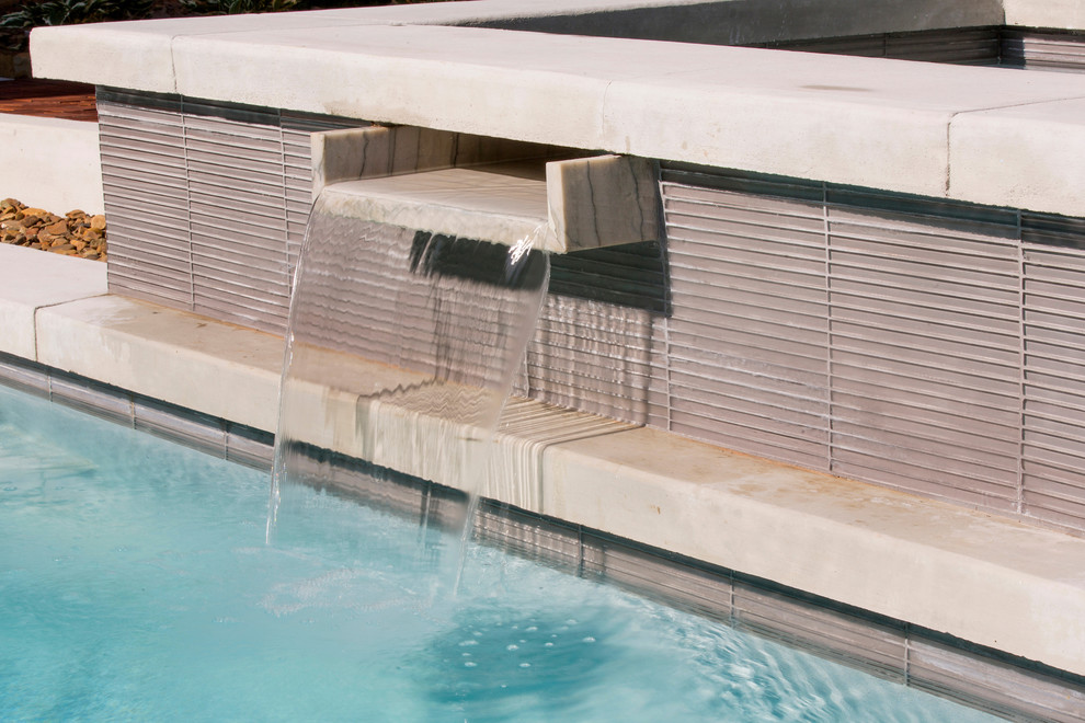 Modelo de piscina con fuente alargada tradicional de tamaño medio en patio trasero con losas de hormigón