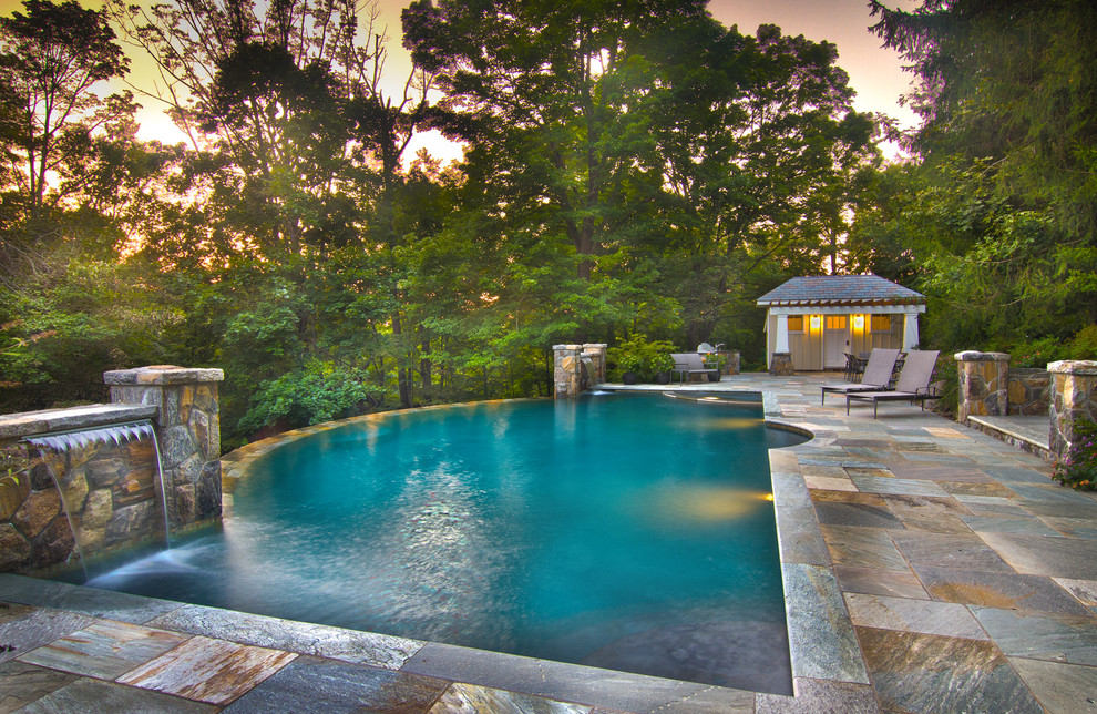 Immagine di una grande piscina a sfioro infinito stile americano personalizzata dietro casa con fontane e pavimentazioni in pietra naturale