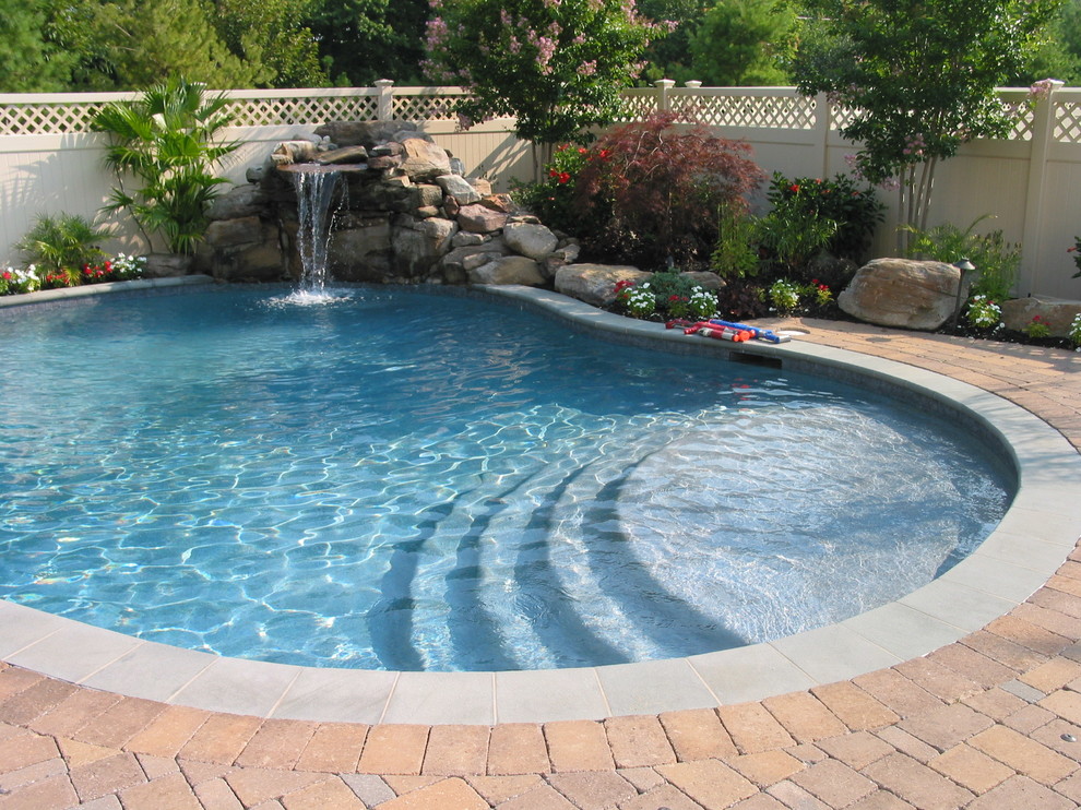 Modelo de piscina con fuente natural tradicional de tamaño medio tipo riñón en patio trasero con adoquines de hormigón