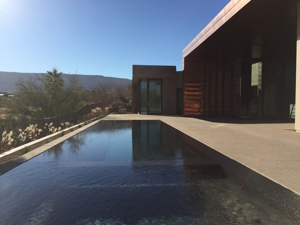 Modelo de piscina alargada minimalista grande rectangular en patio trasero con losas de hormigón