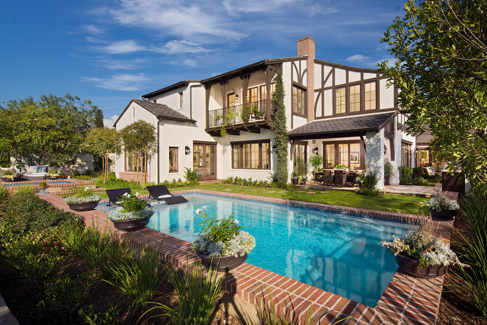 Farmhouse back rectangular swimming pool in Orange County with brick paving.