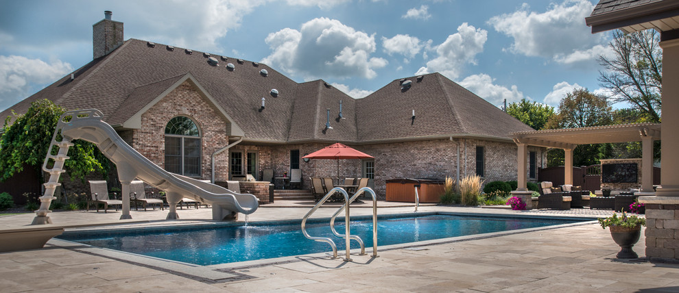 Modelo de casa de la piscina y piscina alargada clásica de tamaño medio rectangular en patio trasero con adoquines de piedra natural