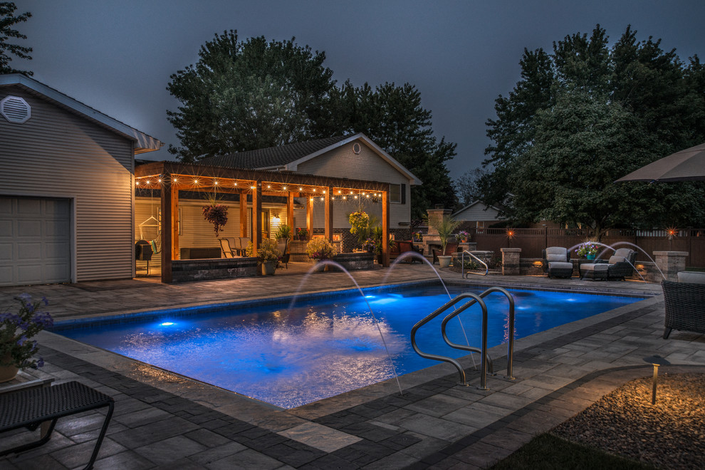 Ejemplo de casa de la piscina y piscina alargada clásica de tamaño medio rectangular en patio trasero con adoquines de hormigón