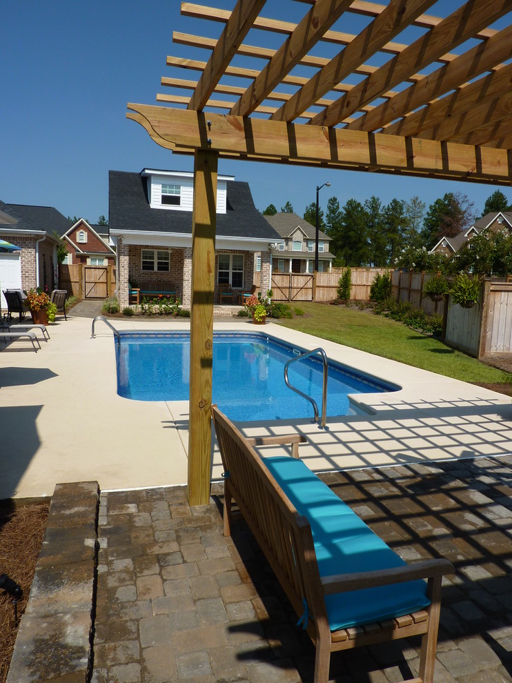 Imagen de piscina alargada clásica de tamaño medio rectangular en patio trasero con losas de hormigón