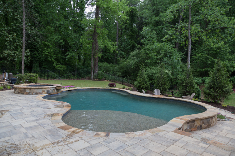 Ispirazione per una piscina naturale tradizionale personalizzata di medie dimensioni e dietro casa con una vasca idromassaggio e pavimentazioni in cemento