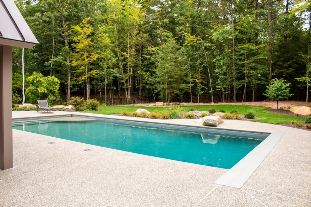 Large rural side rectangular natural swimming pool in Boston with a pool house and decking.