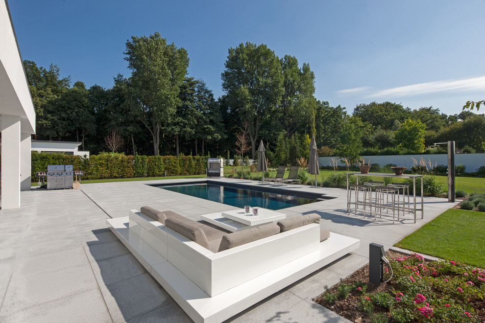Imagen de piscina actual de tamaño medio rectangular en patio trasero con losas de hormigón