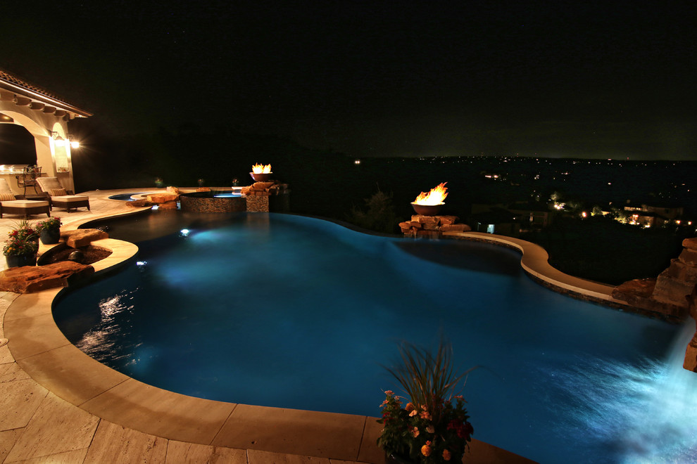 Immagine di un'ampia piscina a sfioro infinito mediterranea personalizzata dietro casa con un acquascivolo e pavimentazioni in pietra naturale