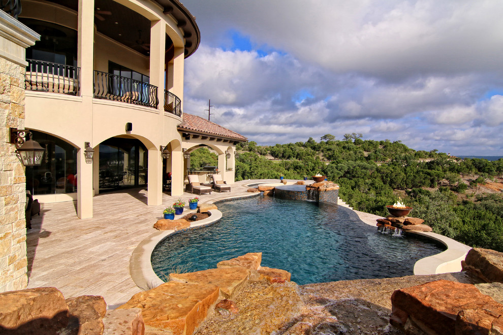 Ispirazione per un'ampia piscina a sfioro infinito mediterranea personalizzata dietro casa con un acquascivolo e pavimentazioni in pietra naturale