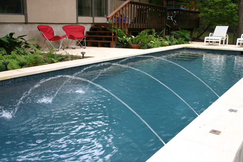 Modelo de piscina alargada tradicional de tamaño medio rectangular en patio trasero con adoquines de piedra natural