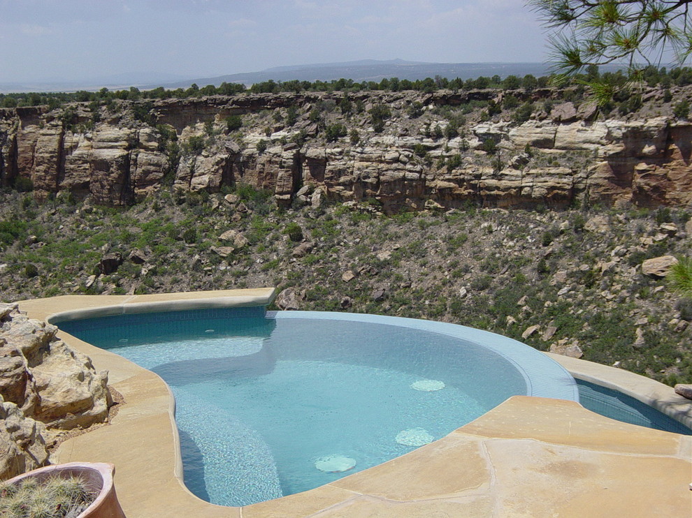 Ispirazione per un'ampia piscina a sfioro infinito stile americano personalizzata dietro casa con una vasca idromassaggio e pavimentazioni in pietra naturale