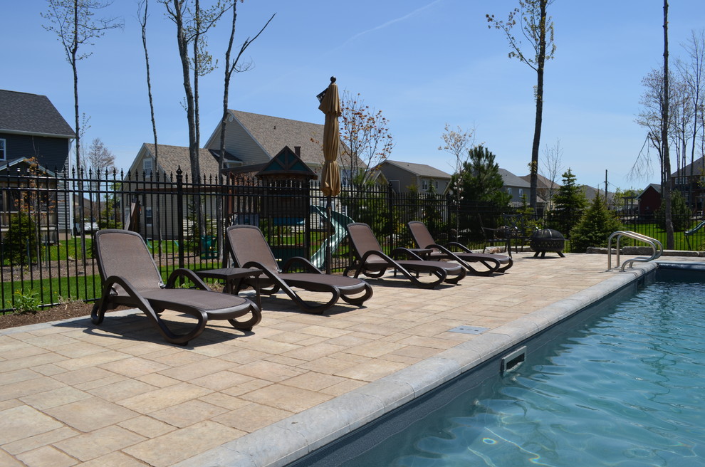 Modelo de piscina actual de tamaño medio rectangular en patio trasero con adoquines de hormigón