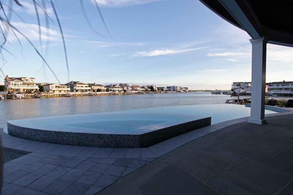 Foto di una grande piscina a sfioro infinito stile marino personalizzata dietro casa con una vasca idromassaggio e piastrelle