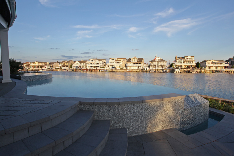 Foto di una grande piscina a sfioro infinito costiera personalizzata dietro casa con una vasca idromassaggio e piastrelle