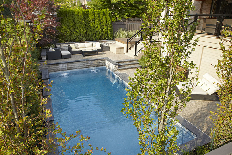 Ejemplo de piscina con fuente natural minimalista grande rectangular en patio trasero con losas de hormigón