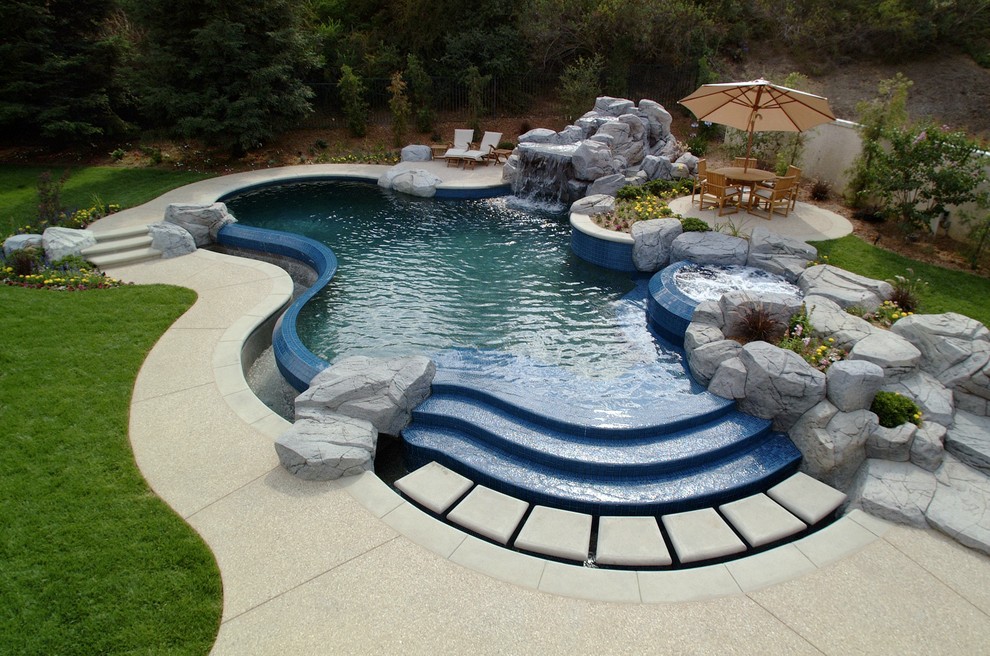 Immagine di una grande piscina a sfioro infinito tradizionale personalizzata dietro casa con fontane e cemento stampato