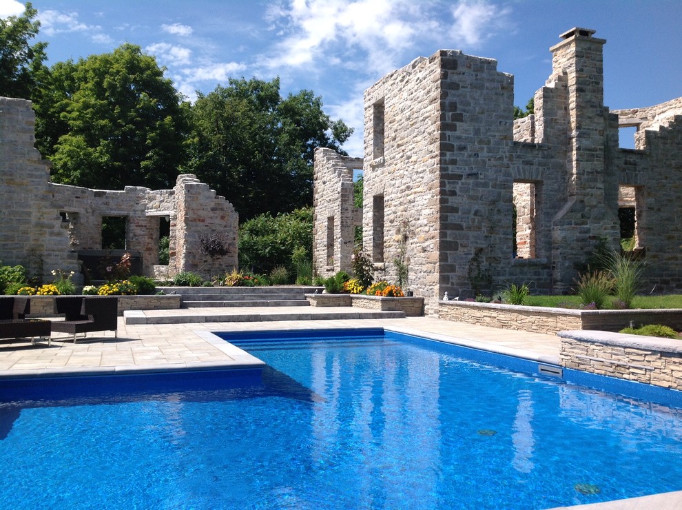 Foto de piscina con fuente natural tradicional grande en forma de L en patio trasero con adoquines de hormigón