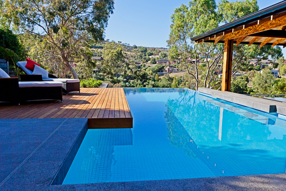 Diseño de piscina infinita de tamaño medio rectangular en patio trasero con entablado