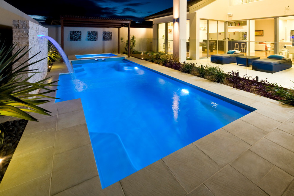 Ejemplo de piscina con fuente de tamaño medio rectangular en patio trasero con adoquines de piedra natural