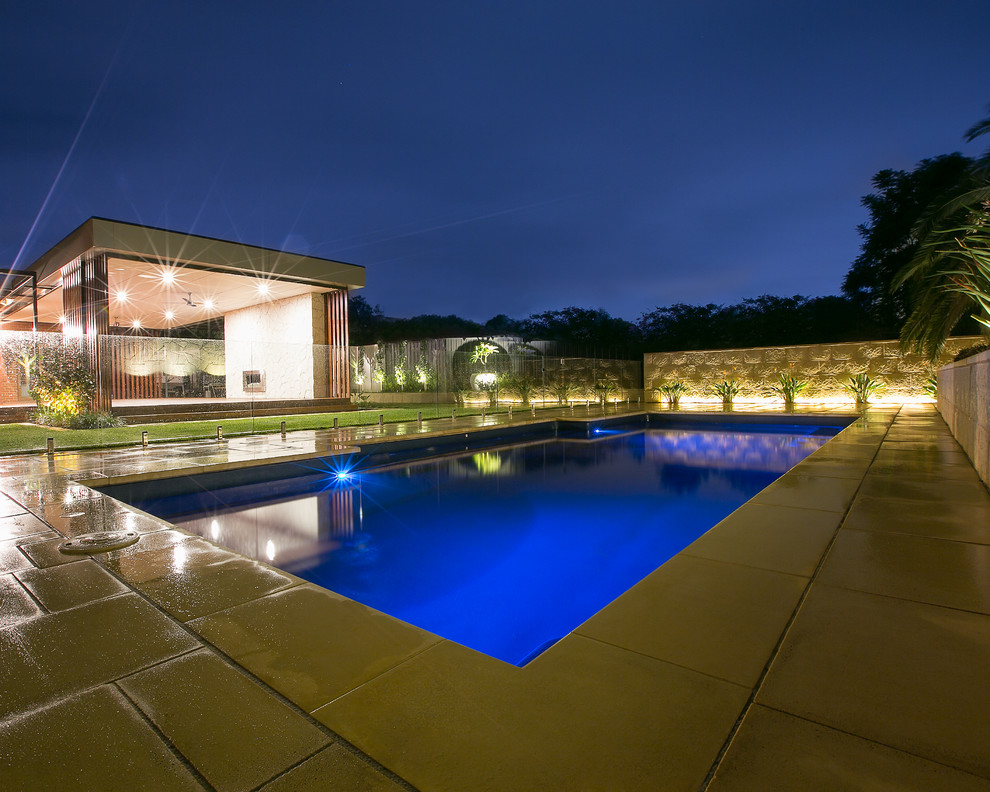 Modelo de piscina moderna de tamaño medio rectangular en patio trasero con adoquines de piedra natural