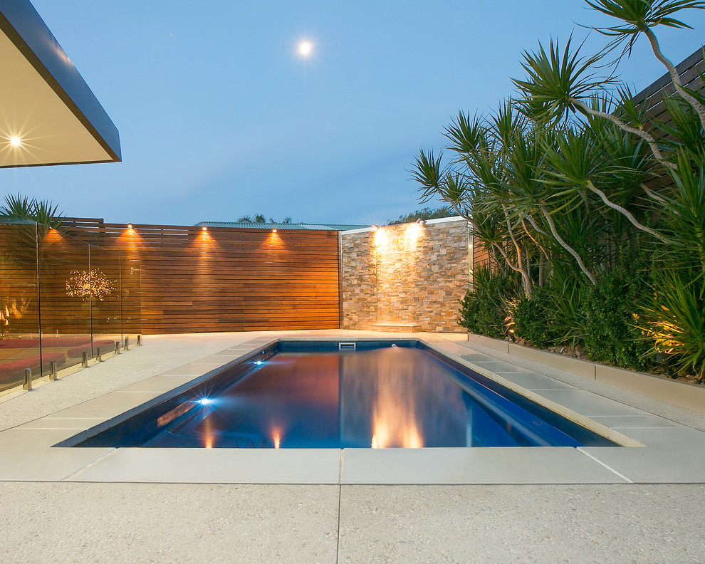Immagine di una piscina minimalista rettangolare di medie dimensioni e dietro casa con lastre di cemento