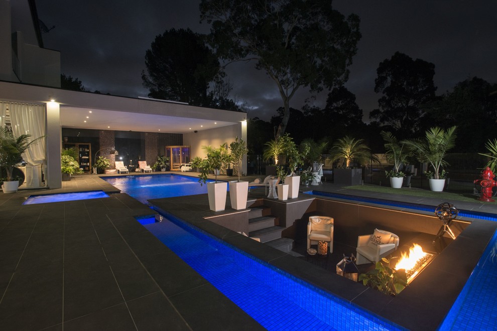Ejemplo de piscina minimalista grande a medida en patio trasero con adoquines de piedra natural