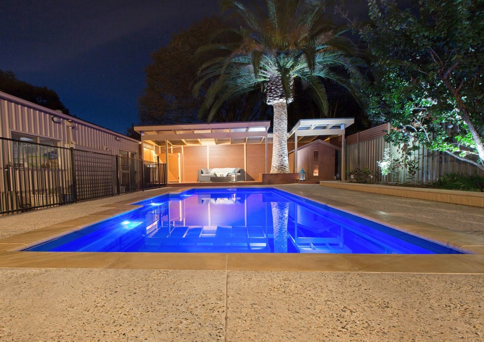 Modelo de piscina actual de tamaño medio rectangular en patio trasero con losas de hormigón