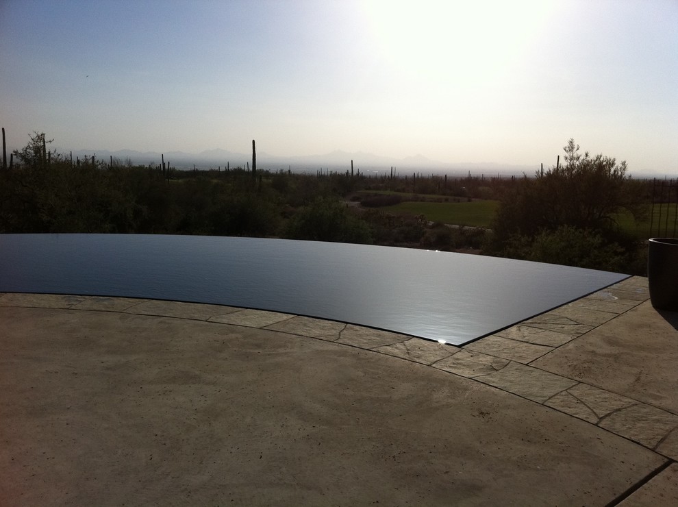 Immagine di una piscina a sfioro infinito design personalizzata di medie dimensioni e dietro casa con una vasca idromassaggio e lastre di cemento