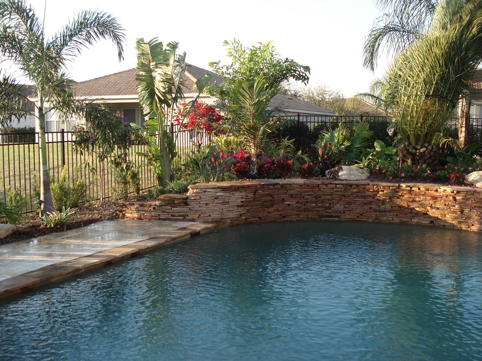 Modelo de piscina con fuente natural tropical de tamaño medio a medida en patio trasero con adoquines de ladrillo