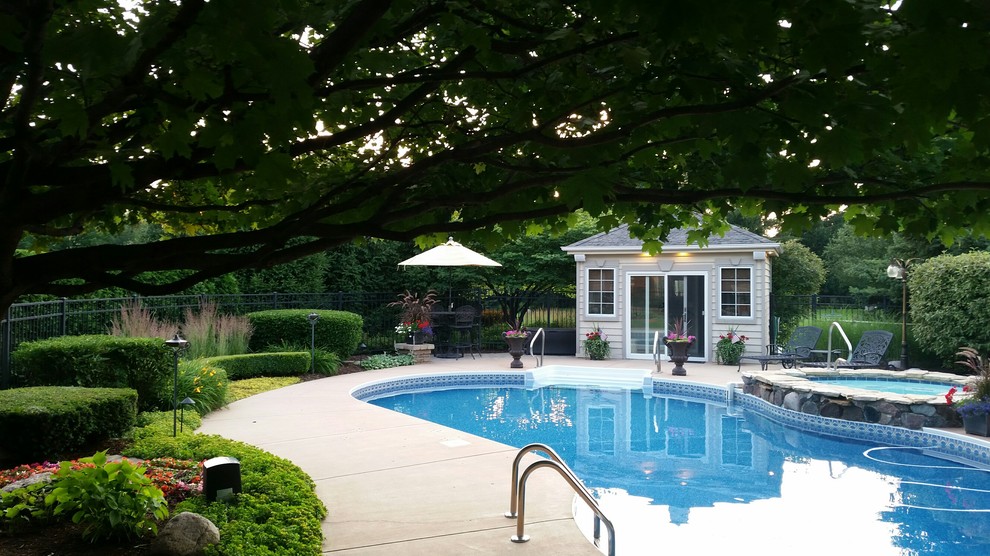 Foto di una grande piscina classica a "C" dietro casa con lastre di cemento e una vasca idromassaggio