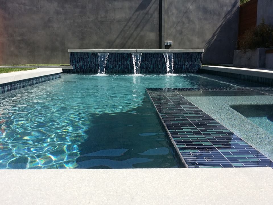 Ejemplo de piscina con fuente minimalista de tamaño medio en forma de L en patio trasero con adoquines de hormigón