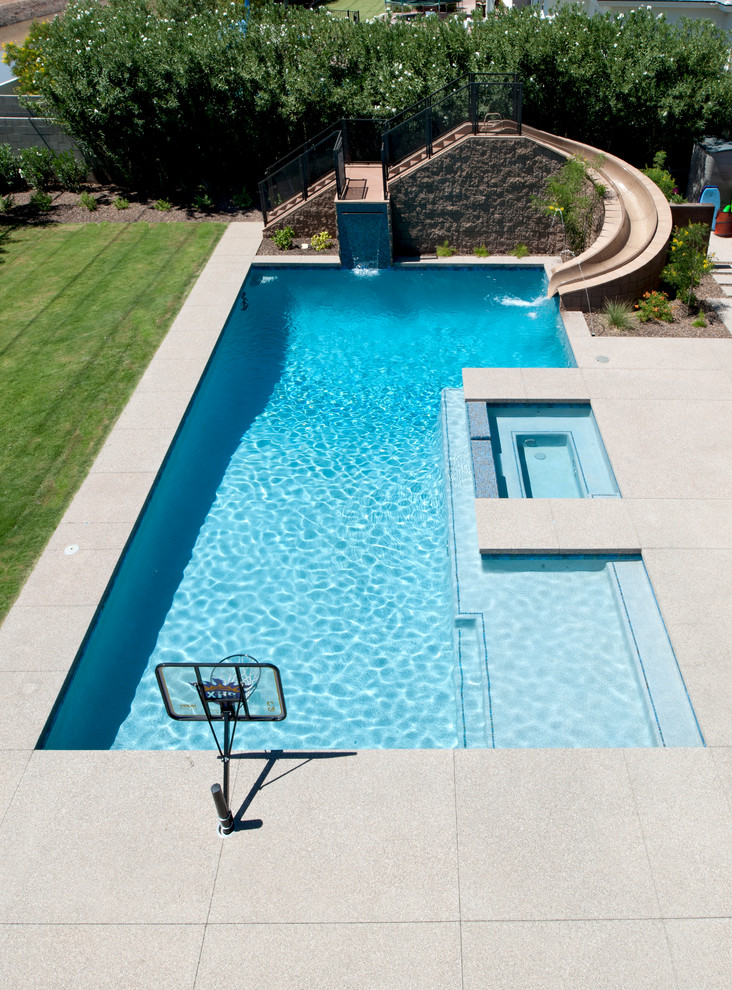 Ejemplo de piscina con tobogán actual de tamaño medio rectangular en patio trasero con adoquines de hormigón
