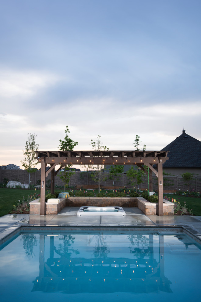 Immagine di una grande piscina monocorsia classica rettangolare dietro casa con lastre di cemento e una vasca idromassaggio