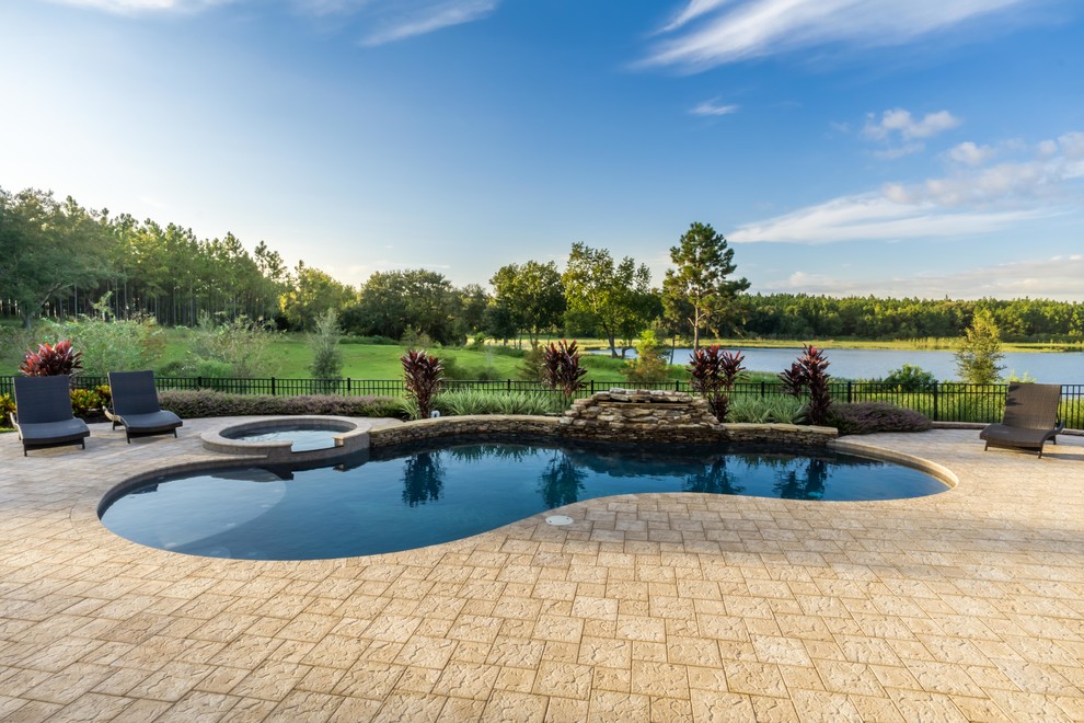 Immagine di una piscina naturale chic personalizzata di medie dimensioni e dietro casa con pavimentazioni in pietra naturale e una vasca idromassaggio