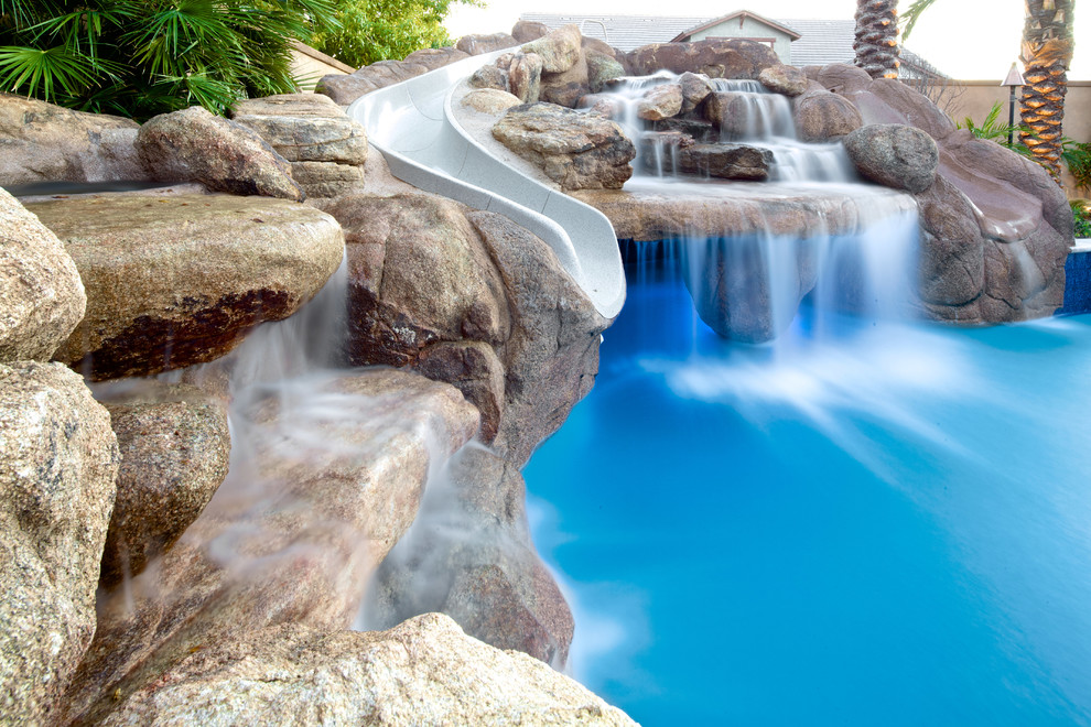 Diseño de piscina natural mediterránea grande a medida en patio trasero con adoquines de piedra natural