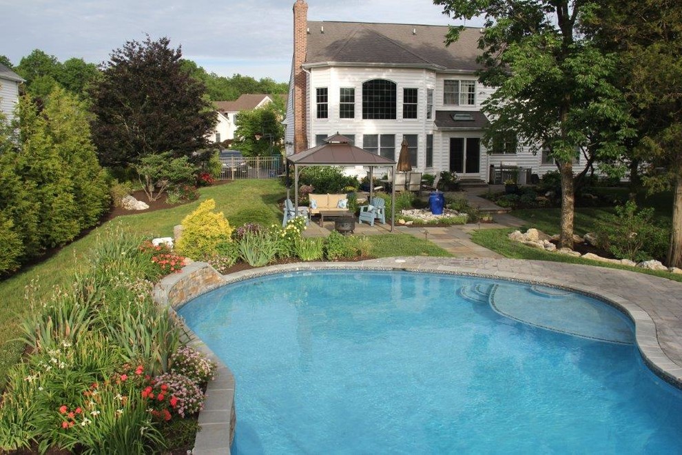 Modelo de piscina con tobogán alargada tradicional grande tipo riñón en patio trasero con adoquines de piedra natural