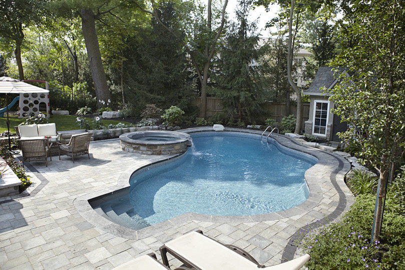 This is an example of a large contemporary back custom shaped natural swimming pool in Toronto with a water feature and brick paving.
