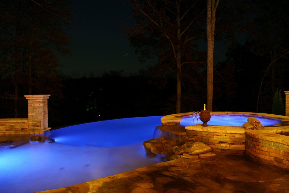 Example of a large classic backyard stone and custom-shaped infinity hot tub design in Atlanta