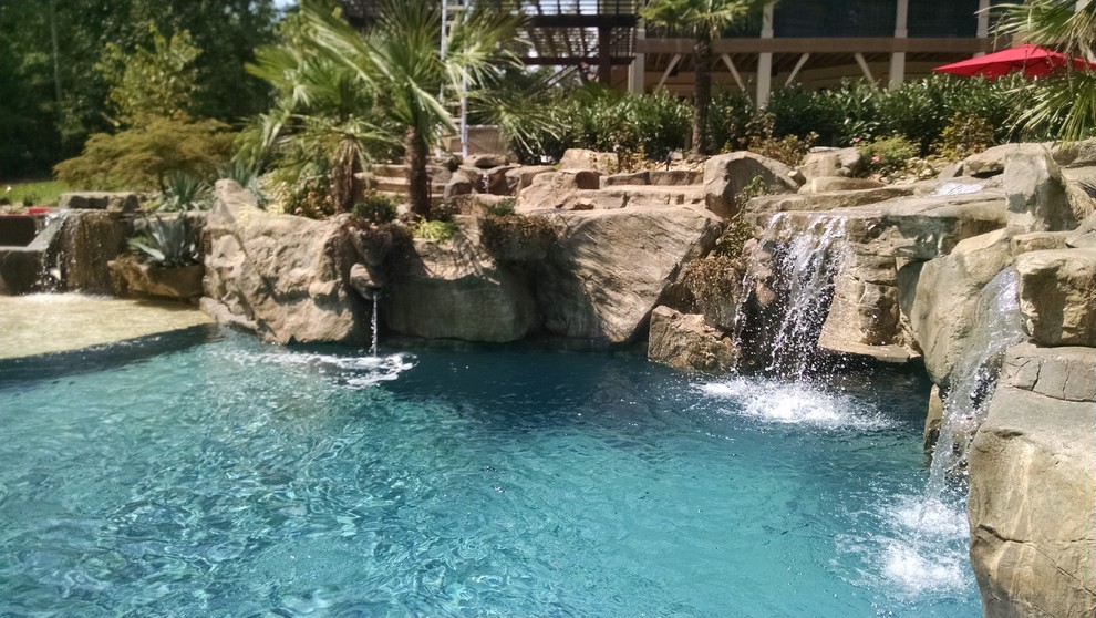 Esempio di una grande piscina tropicale personalizzata dietro casa con pavimentazioni in pietra naturale e un acquascivolo