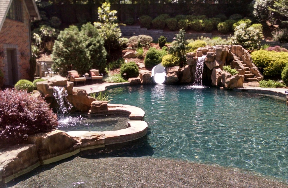 На фото: большой бассейн произвольной формы на заднем дворе в современном стиле с покрытием из каменной брусчатки и водной горкой с