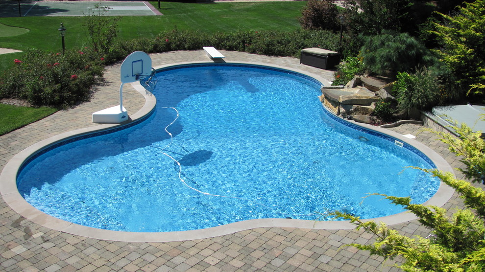 Exempel på en klassisk anpassad pool på baksidan av huset, med en fontän och marksten i tegel