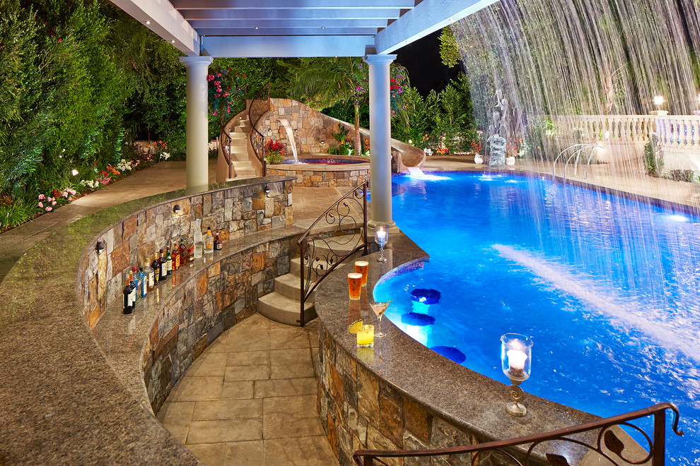 На фото: большой естественный бассейн произвольной формы на заднем дворе в средиземноморском стиле с водной горкой и покрытием из декоративного бетона