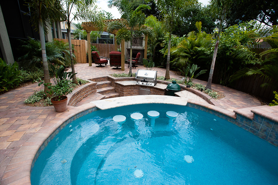 Exempel på en mellanstor exotisk njurformad pool på baksidan av huset, med en fontän och marksten i tegel