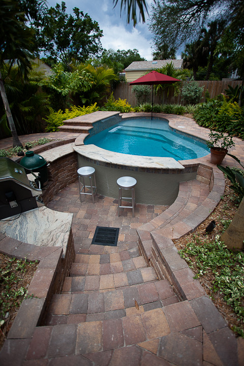 Imagen de piscina con fuente tropical de tamaño medio tipo riñón en patio trasero con adoquines de ladrillo