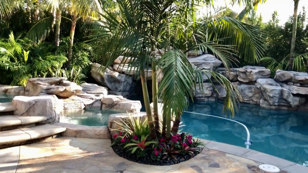 Ejemplo de piscina con fuente natural tropical grande en patio trasero