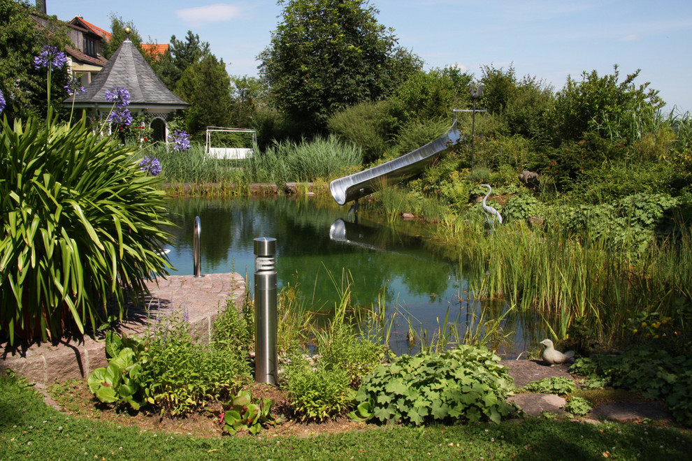 Mittelgroßer Klassischer Schwimmteich neben dem Haus in individueller Form mit Wasserrutsche und Natursteinplatten in Stuttgart