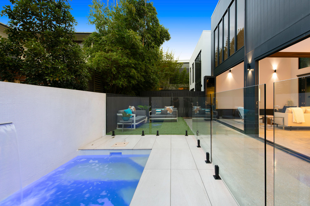Ejemplo de piscina alargada actual de tamaño medio rectangular en patio trasero con adoquines de piedra natural