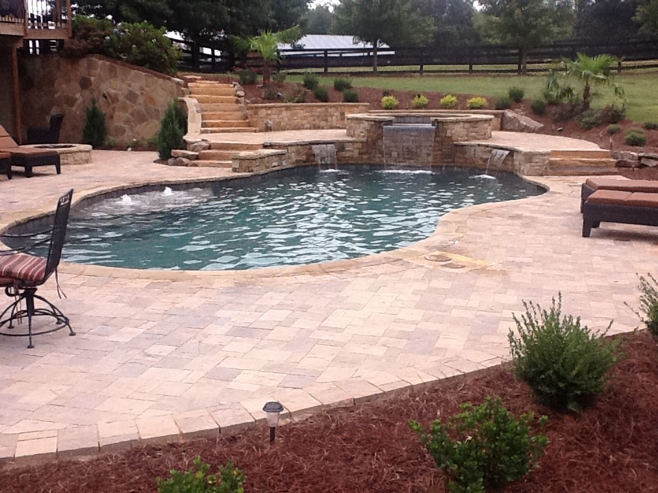 Diseño de piscina con fuente natural rural grande a medida en patio trasero con adoquines de piedra natural