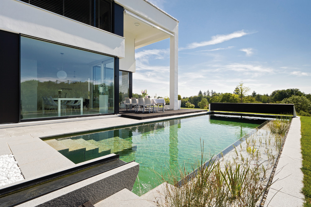Mittelgroßer Moderner Schwimmteich hinter dem Haus in rechteckiger Form mit Betonplatten in München