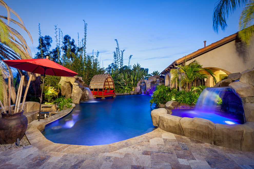Idee per un'ampia piscina naturale tropicale personalizzata dietro casa con pavimentazioni in pietra naturale e fontane